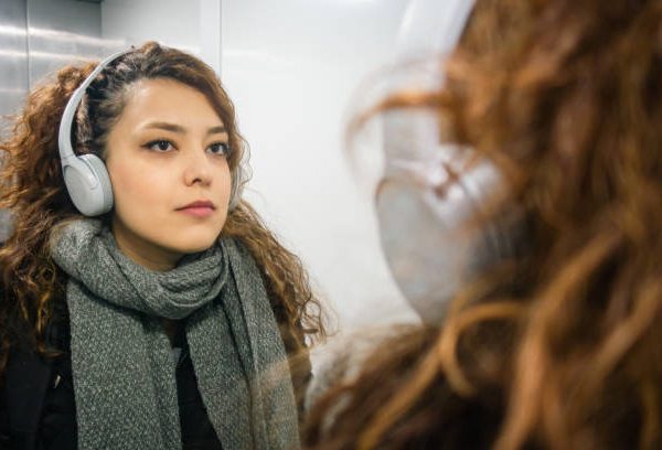 Beautiful young woman with headphones in elevator with reflection in mirror during winter
