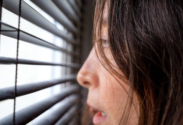 Head of a young woman afraid looking through venetian blinds on a window