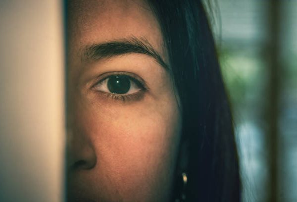 Partial view of a dark-haired woman hiding and spying behind the door