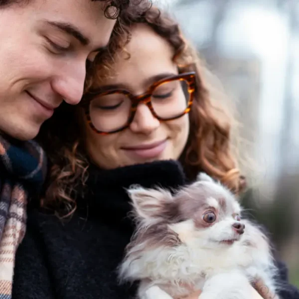 Young smiling couple holding together a white and gray chihuahua outdoors